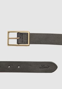 Ceinture en cuir noir avec une boucle rectangulaire dorée et un petit logo Levi's embossé près de l'extrémité pointue sur un fond clair.