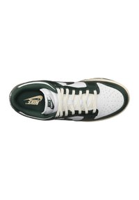 Sneaker Nike con tomaia in pelle bianca e accenti verdi, dotata di punta perforata, lacci piatti beige e logo sulla linguetta.
