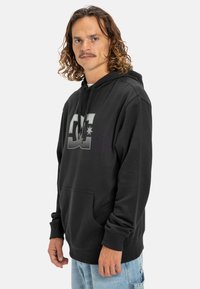 Čierna bavlnená mikina s klokanním vreckom, kapucňou na šnúrku a štruktúrovanou potlačou loga na prednej strane. Voľný, uvoľnený strih.