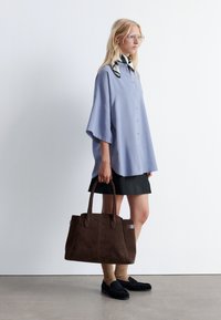 Light blue oversized button-up shirt, black skirt, brown suede tote bag, brown socks, and black loafers. Minimalist design with contrasting colors.