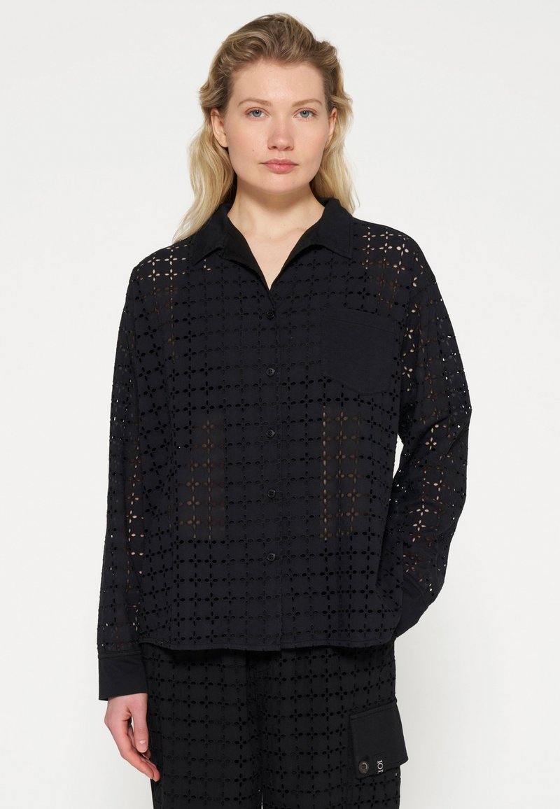 Zwarte eyelet blouse met knopen, voorzien van een kraag, lange mouwen en een borstzak, met een gelaagd uitgesneden bloemenpatroon en textuurstof.
