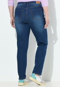 Jeans de mezclilla azul oscuro con cinturilla, que presentan dos bolsillos traseros y costuras en contraste. Combinados con zapatillas multicolores.