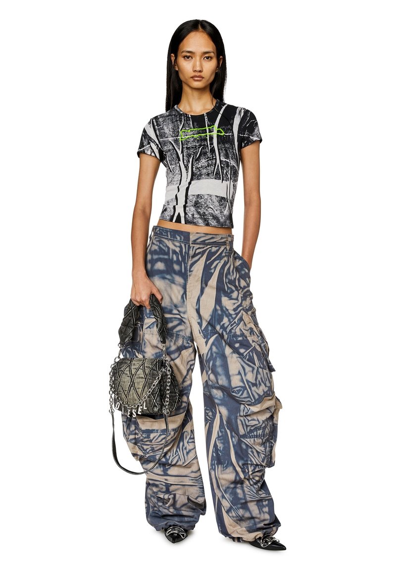 Black and white graphic cropped shirt with green detailing, paired with loose, patterned beige-blue cargo pants and a textured black bag.