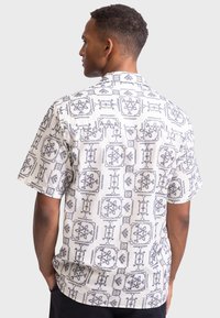 Short-sleeve shirt in white fabric featuring a navy geometric floral pattern, with a relaxed fit and a notched collar.