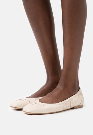 Ballerines en cuir beige avec un bout rond et un détail froncé le long des bords. Semelle texturée et design minimaliste.