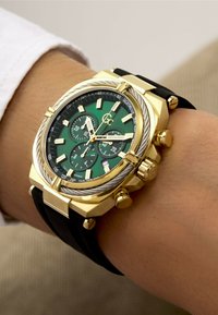 Gold-tone chronograph watch featuring a green dial, black rubber strap, textured bezel, and silver accents on dials and hands.