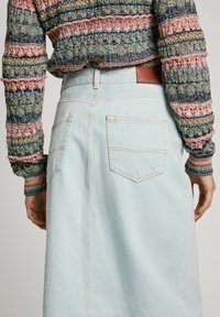 Lyseblå denimskjørt med to baklommer, sømdetaljer og et brunt l�ærmerke ved livlinjen, kombinert med en flerfarget mønstret genser.