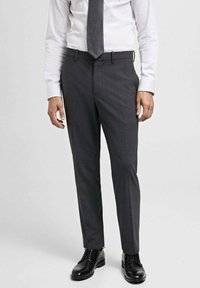 Sive krojene hlače od glatke tkanine, sa slim fit krojem, bočnim džepovima i petljama za remen, uparene s crnim cipelama.