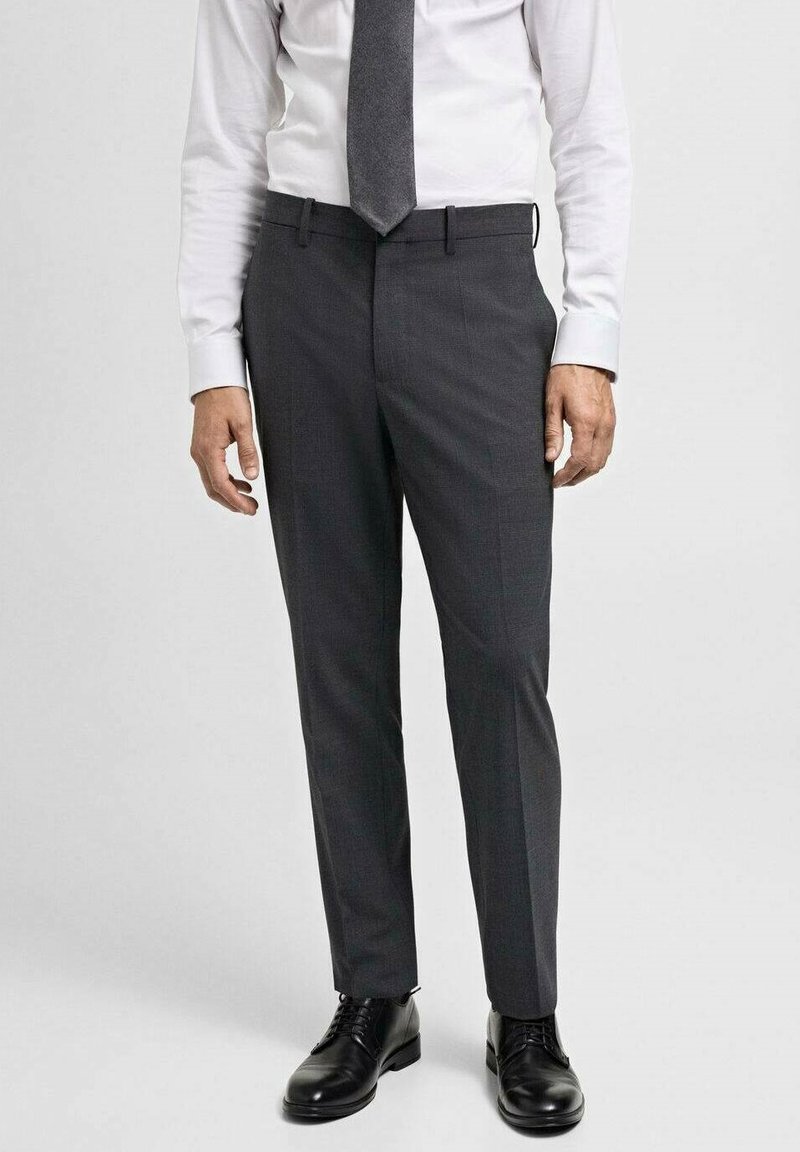 Sive krojene hlače od glatke tkanine, sa slim fit krojem, bočnim džepovima i petljama za remen, uparene s crnim cipelama.