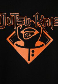 Tessuto nero con un disegno grafico arancione, testo stilizzato "JutsuKai" e simbolo di una mano, che crea un contrasto audace e un'estetica moderna.