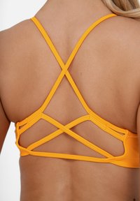 Narančasti sportski grudnjak s leđa s dizajnom križanja, napravljen od rastezljivog materijala s glatkom teksturom koja ističe detalje leđa.