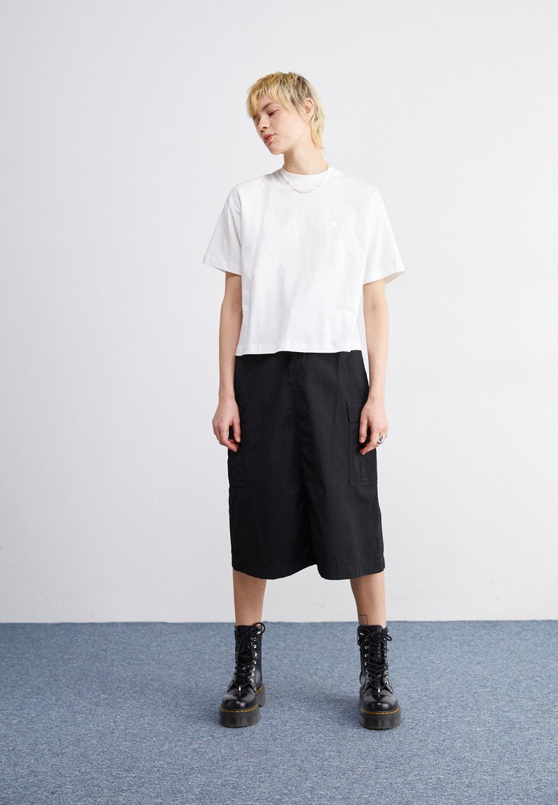 T-shirt cropped bianco in cotone abbinato a una gonna cargo nera fino al ginocchio e stivali alla caviglia neri con lacci. Design semplice e vestibilità comoda.