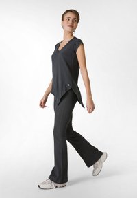 Top negru, cu maneci scurte si decolteu in V, cu tiv asimetric, purtat cu pantaloni negri ajustati cu evazare si adidasi de culoare deschisa.