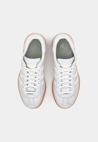 Grå sneakers med en strukturerad ovandel, vita ränder och en brun gummisula. Vita skosnören och en mönstrad grå innersula.