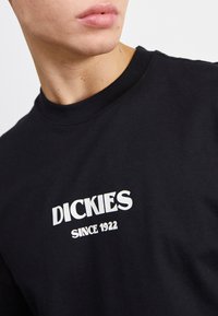Camiseta de algodón negra con un logo blanco "DICKIES SINCE 1922" en la parte frontal. Cuello redondo y mangas cortas con una textura suave.
