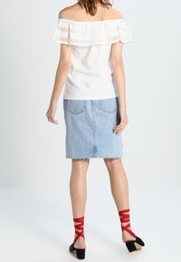 White off-the-shoulder top with lace trim, paired with a light denim skirt and red strappy sandals. Back view showcases layered fabric design.