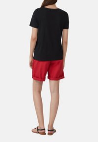 Zwarte T-shirt met korte mouwen gecombineerd met rode opgerolde shorts en zwarte sandaaltjes met bandjes. Focus op een casual, comfortabele kledingstijl.