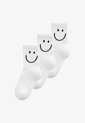 Drei weiße Crew-Socken mit schwarzen Smiley-Gesichtern auf den gerippten Bündchen, diagonal auf weißem Hintergrund angeordnet.