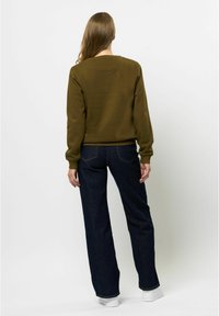 Olivno zelena trenerka s okroglo ovratnikom, rebrastimi manšetami in robom; v kombinaciji s temno modrimi širokimi hlačami in belimi športnimi copati.