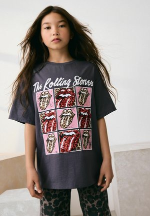 Dunkelgraues, übergroßes T-Shirt mit einem mit Pailletten besetzten Rolling Stones-Logo-Design auf pinkem Hintergrund, kombiniert mit leopardfarbigen Hosen.