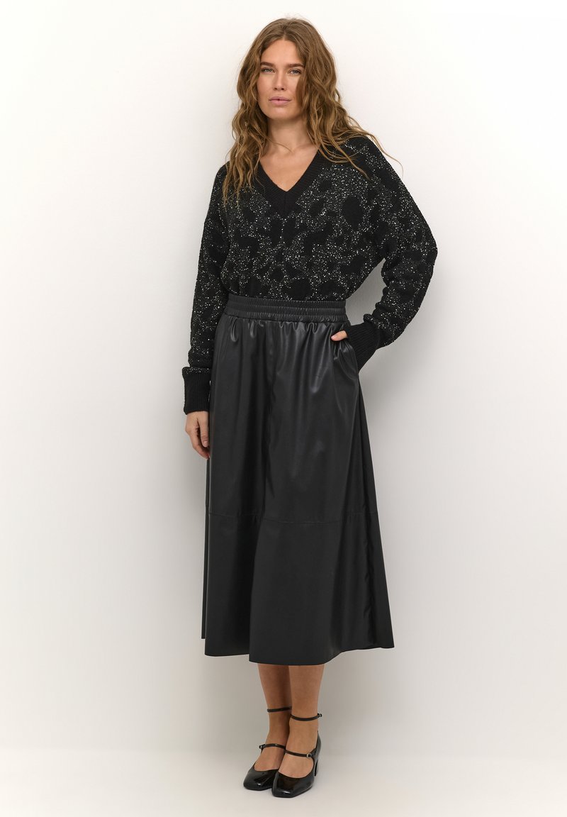 Zwarte gebreide trui met metallic accenten en een V-hals. Een zwart faux leren enkellange rok met een elastische tailleband. Geëmailleerde schoenen.