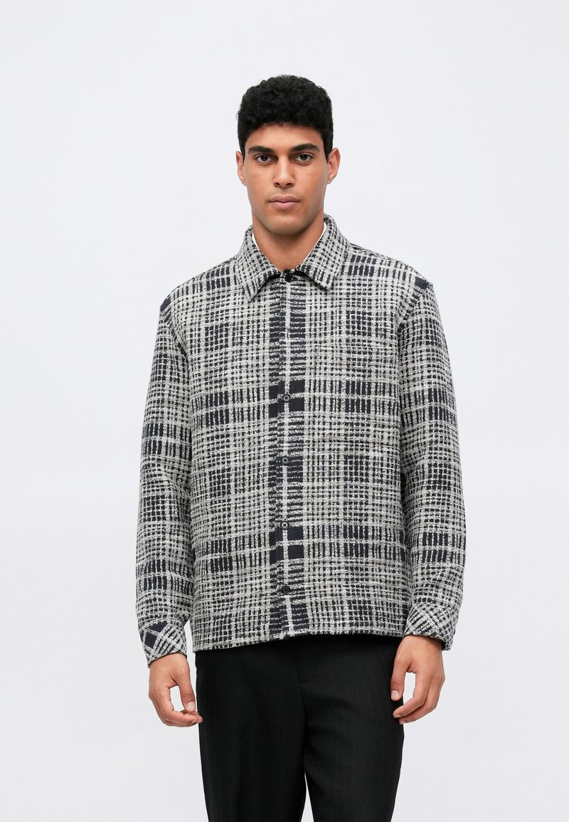 Πουκάμισο με κουμπιά σε γκρι και μαύρο καρό σχέδιο, με γιακά και μακριά μανίκια, φτιαγμένο από υφασματική υφή.