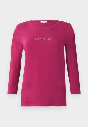 Chemise fuchsia à manches longues avec un col rond et le texte "TOM TAILOR" en strass sur la poitrine. Matière en coton douce.