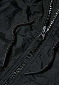 Zwarte zip-up jack met een gestructureerde stof, verstelbare trekkoord capuchon en een stijlvolle zwarte rits met plastic trekknop.