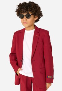 Blazer rosso in tessuto liscio con revers a punta, due bottoni e tasche laterali. Abbinato a una t-shirt bianca semplice e occhiali da sole scuri.