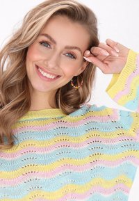 Pull en tricot multicolore avec un motif de vagues en bleu, jaune et rose. Le matériau est léger et a une coupe ample.