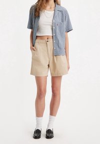 Camisa de manga corta a cuadros en azul y blanco combinada con pantalones cortos beige. El material parece ligero, con bolsillos visibles y un ajuste relajado.