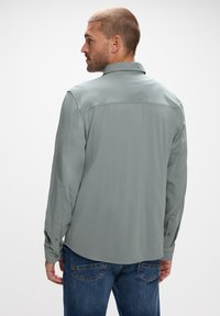 Ljust grå långärmad skjorta med klassisk krage, knappmanschetter och en slät textur, som bärs med blå denimjeans. Baksidan visas.