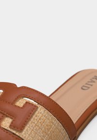 Καφέ δερμάτινο σανδάλι τύπου slide με πλεκτή λεπτομέρεια από άχυρο και ανάγλυφο σχέδιο "Η" στο πάνω μέρος, μπεζ εσωτερική σόλα με το όνομα της μάρκας.