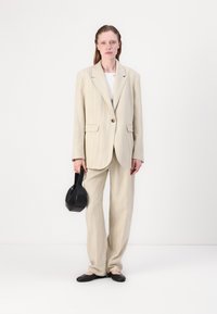Lichtbeige streepjespak met een blazer met één knoop en wijde broekspijpen, gecombineerd met zwarte flats en een zwarte handtas.
