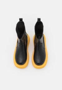 Botas tobilleras de cuero negro con un acabado texturizado, que cuentan con suela de goma amarilla y paneles laterales elásticos para facilitar su uso.