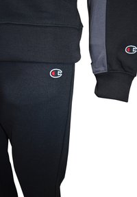 Mörk fleece-tröja och sweatpants-set. Tröjan har ribbade muddspartier, byxorna har resårmidja, båda med en logodetalj i rött och vitt.