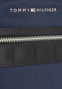 Tessuto blu navy con un cinturino nero e una zip bianca. Un logo del brand argentato reca la scritta "TOMMY HILFIGER" sopra la zip.