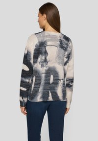 Strickpullover mit einem großen abstrakten schwarzen und grauen Grafikdesign auf hellem Hintergrund. Lange Ärmel und Rundhalsausschnitt.