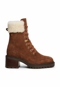 Botín de ante marrón con cordones, forrado de pelo sintético, accesorios en dorado y un grueso tacón cuadrado. Suela de goma texturizada para un buen agarre.