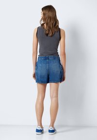 Džínové šortky s přiléhavým pasem a postranními kapsami. Modrá barva, roztrhaný lem, nošeny se šedým tílkem a modrými teniskami.