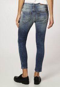 Vybledlé modré skinny džíny s vysokým pasem, se dvěma zadními kapsami a mírným efektem vyblednutí, kombinované s černými botami.