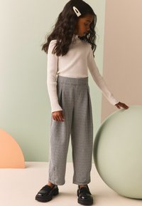 Top blanco de manga larga con canalé y pantalones de cuadros grises de cintura alta. Zapatos negros gruesos. Cabello adornado con un clip de pelo de cuentas.