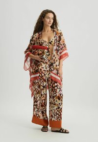 Lichte, doorschijnende kimono met luipaardprint en rode accenten, gecombineerd met wijde broeken en een bijpassende clutch, met een gedurfde kleurenpalet.