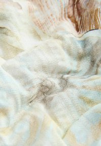 Tissu doux et texturé avec un motif de tons beige clair, brun et bleu pâle, montrant des plis et des détails subtils tissés.