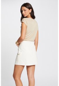 Beige top met korte mouwen, gecombineerd met een witte denim rok met een zakdetail. Glad stoffen textuur met een relaxte pasvorm.