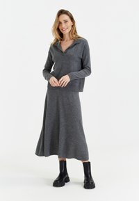 Pull en maille gris avec un col, associé à une jupe grise assortie. Le modèle porte des bottes à semelles épaisses noires. Texture lisse et coupe décontractée.