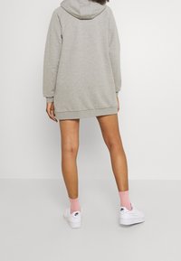 Šedé oversized mikinové šaty s kapucí na stahovací šňůrku, žebrovanými manžetami a lemy. V kombinaci s bílými teniskami a růžovými ponožkami.