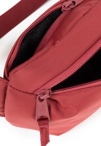 Röd, texturerad tygpåse med dragkedja. Har ett mjukt svart foder och ett hållbart handtag. Dragkedjan har en matchande röd dragrems.