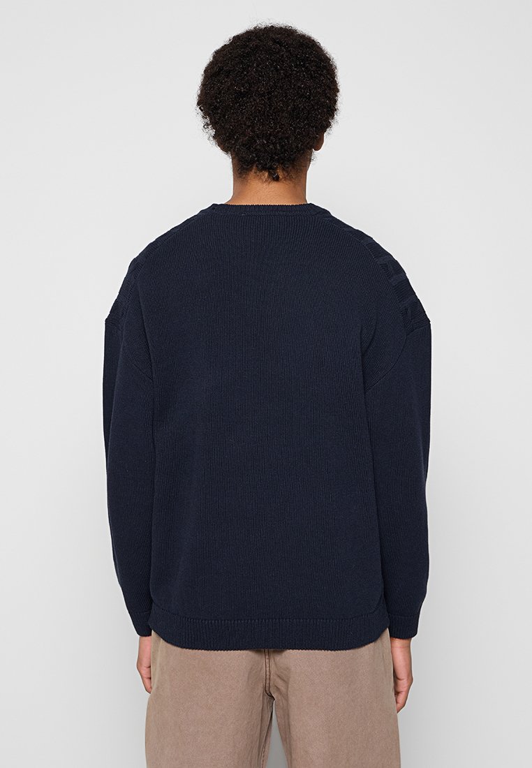 Marineblau gestrickter Pullover mit geripptem Muster, Rundhalsausschnitt und überschnittenen Schultern. Verfügt über kleine Schulterakzente. Einfarbig ohne Muster.