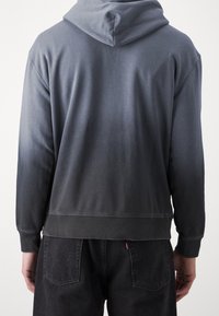 Felpa con cappuccio in gradiente grigio, realizzata in tessuto morbido, con una vestibilità rilassata e con polsini e orlo a coste. Dettaglio della tasca non visibile.